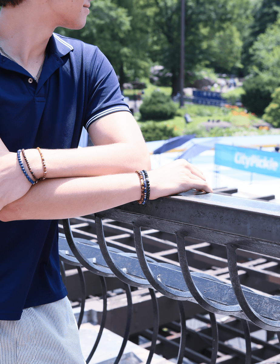 Man wearing a black onyx bracelet with sterling silver zodiac spacer beads, enjoying a sunny day outdoors.