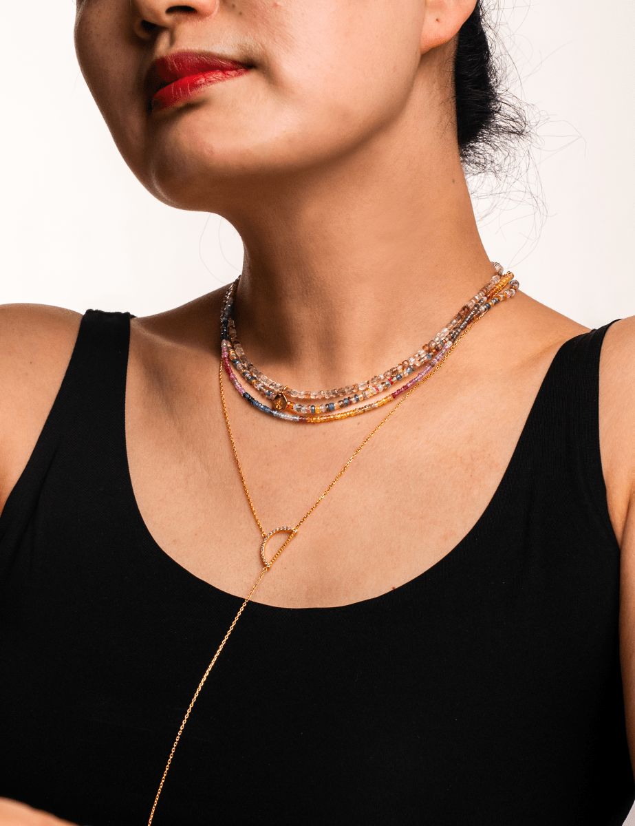 Close-up of a woman wearing a rainbow sapphire necklace with vibrant colors, showcasing its beautiful faceted beads.