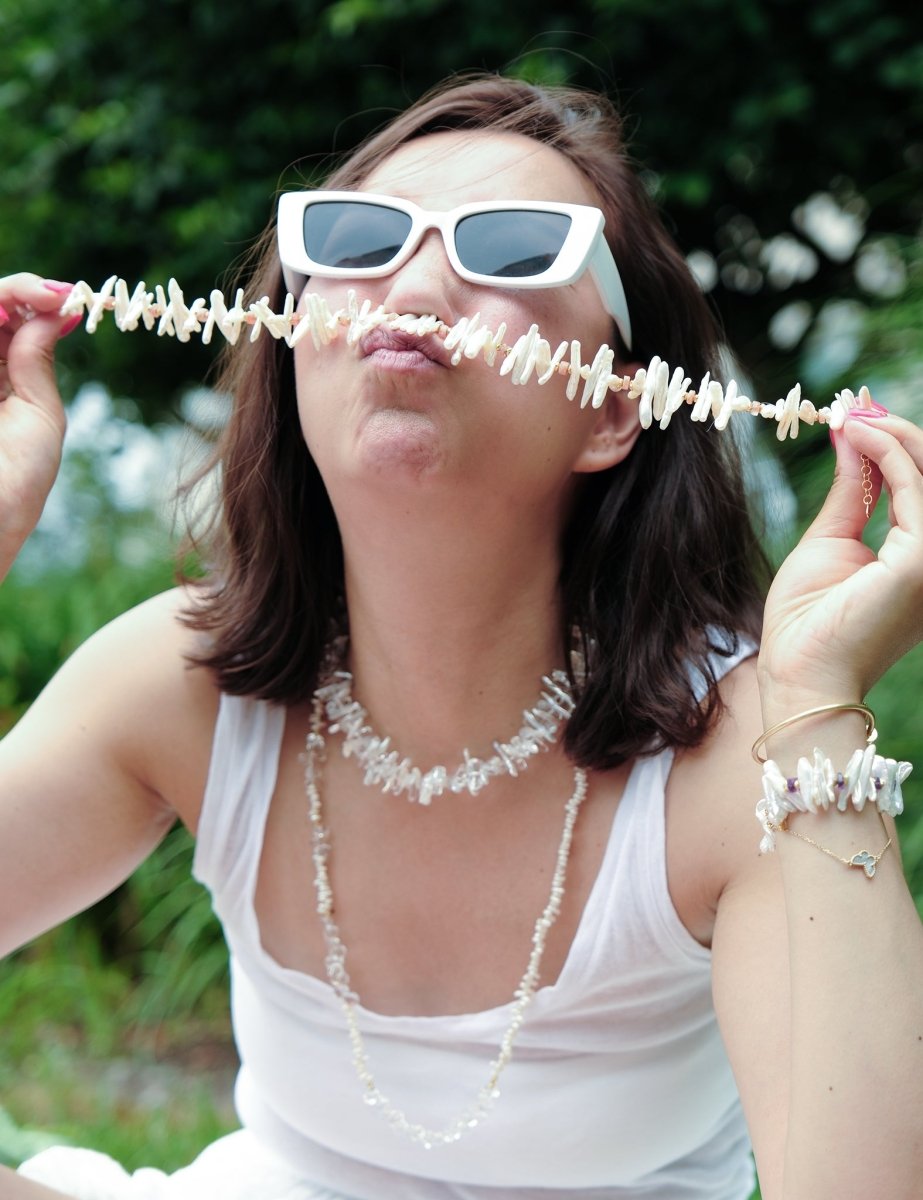 Model wearing sunglasses showcasing a handcrafted pearl necklace, playfully holding it in front of her face.