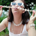 Model wearing sunglasses showcasing a handcrafted pearl necklace, playfully holding it in front of her face.