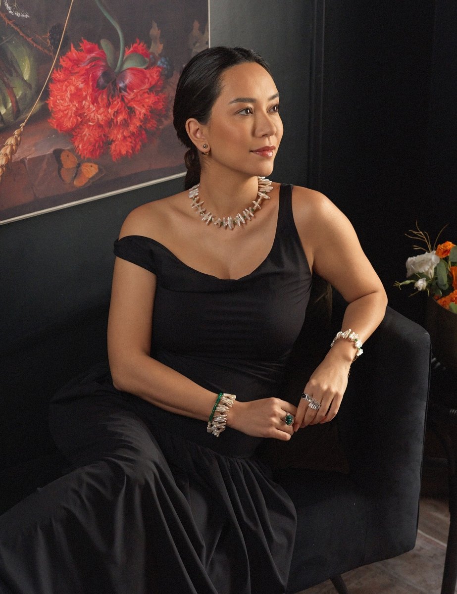 Woman in a black dress with Biwa-style pearl necklace, showcasing elegance and style, against a floral backdrop.