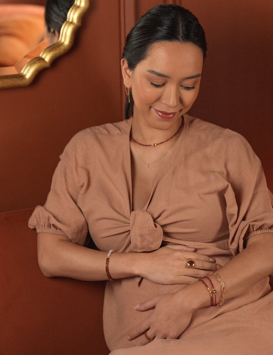 Woman wearing AURA DUO Orange Garnet Pearl Bracelet with elegant attire, showcasing jewelry against a warm background.