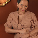 Woman wearing AURA DUO Orange Garnet Pearl Bracelet with elegant attire, showcasing jewelry against a warm background.