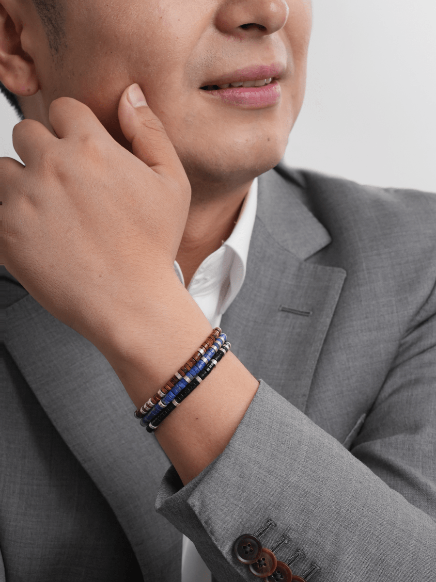 Man wearing Lapis Lazuli and Black Onyx bracelet, showcasing elegance and style in a grey suit.