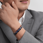 Man wearing Lapis Lazuli and Black Onyx bracelet, showcasing elegance and style in a grey suit.