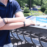Man wearing a black onyx bracelet with sterling silver zodiac spacer beads, enjoying a sunny day outdoors.