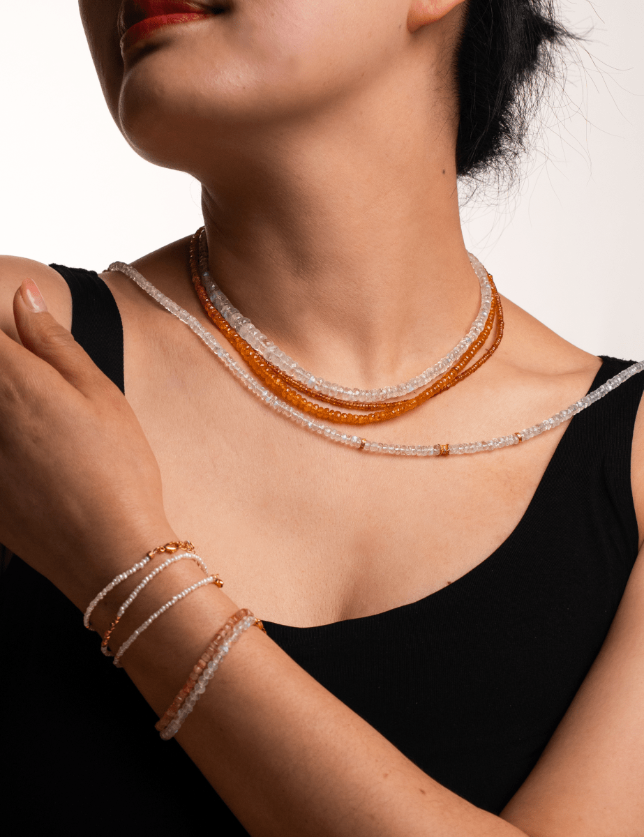 Model wearing layered necklace and bracelets made of faceted moonstone and silver spacer beads, showcasing elegance and style.