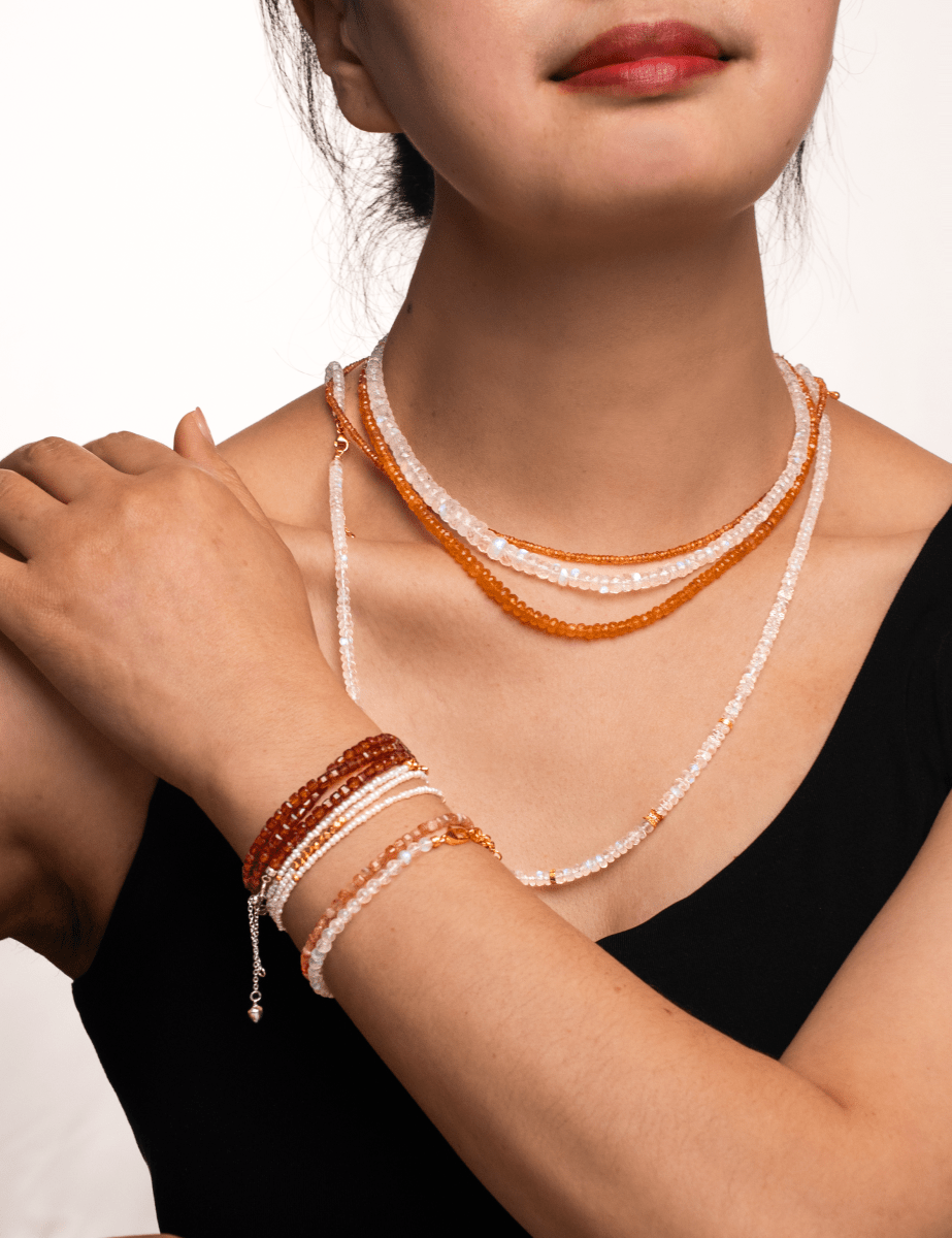 Woman wearing layered moonstone and orange beads necklace with matching bracelets for a chic look.