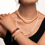 Woman wearing layered moonstone and orange beads necklace with matching bracelets for a chic look.