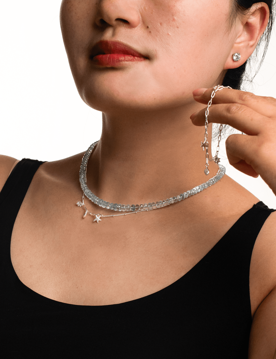 Woman wearing a handcrafted aquamarine faceted necklace with star charms and silver earrings, promoting tranquility.