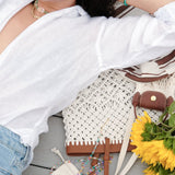 Woman in a white shirt relaxing with a stylish crochet bag, surrounded by sunflowers and colorful accessories.