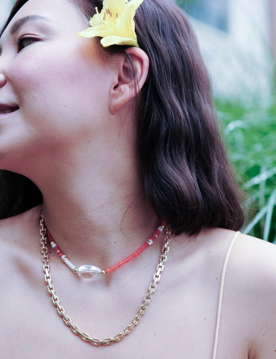 Model wearing MIRA Orange Opal choker necklace, featuring clear quartz and mother of pearl, surrounded by greenery.