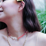 Model wearing MIRA Orange Opal choker necklace, featuring clear quartz and mother of pearl, surrounded by greenery.