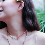 Model wearing MIRA Orange Opal choker necklace, featuring clear quartz and mother of pearl, surrounded by greenery.