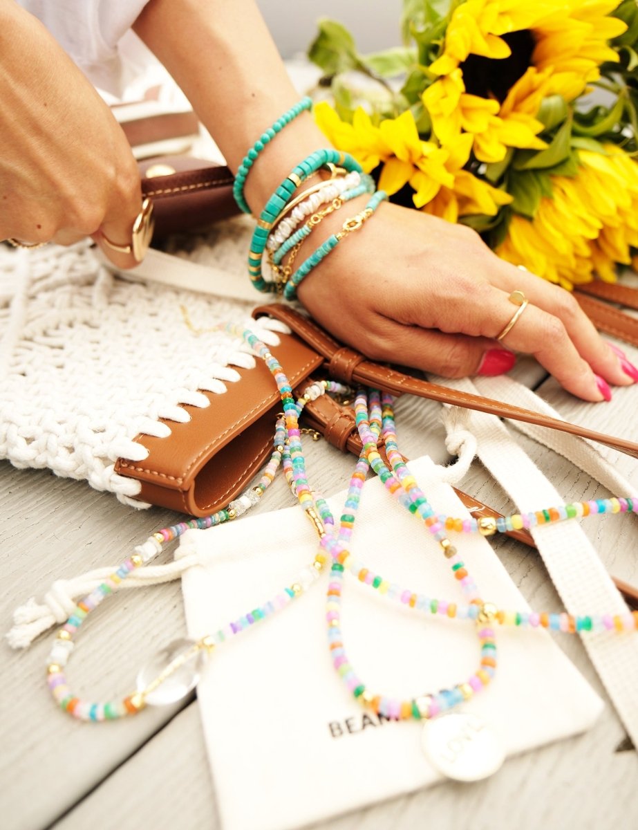 Colorful beaded necklaces and bracelets on a wooden table with sunflowers in the background.