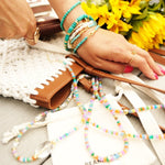 Colorful beaded necklaces and bracelets on a wooden table with sunflowers in the background.