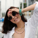 Model wearing stylish sunglasses and layered necklaces in a marina setting, showcasing vibrant colors and accessories.