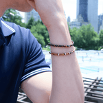 Man wearing a red tiger eye bracelet with silver dice spacer beads, showcasing style in an urban setting.