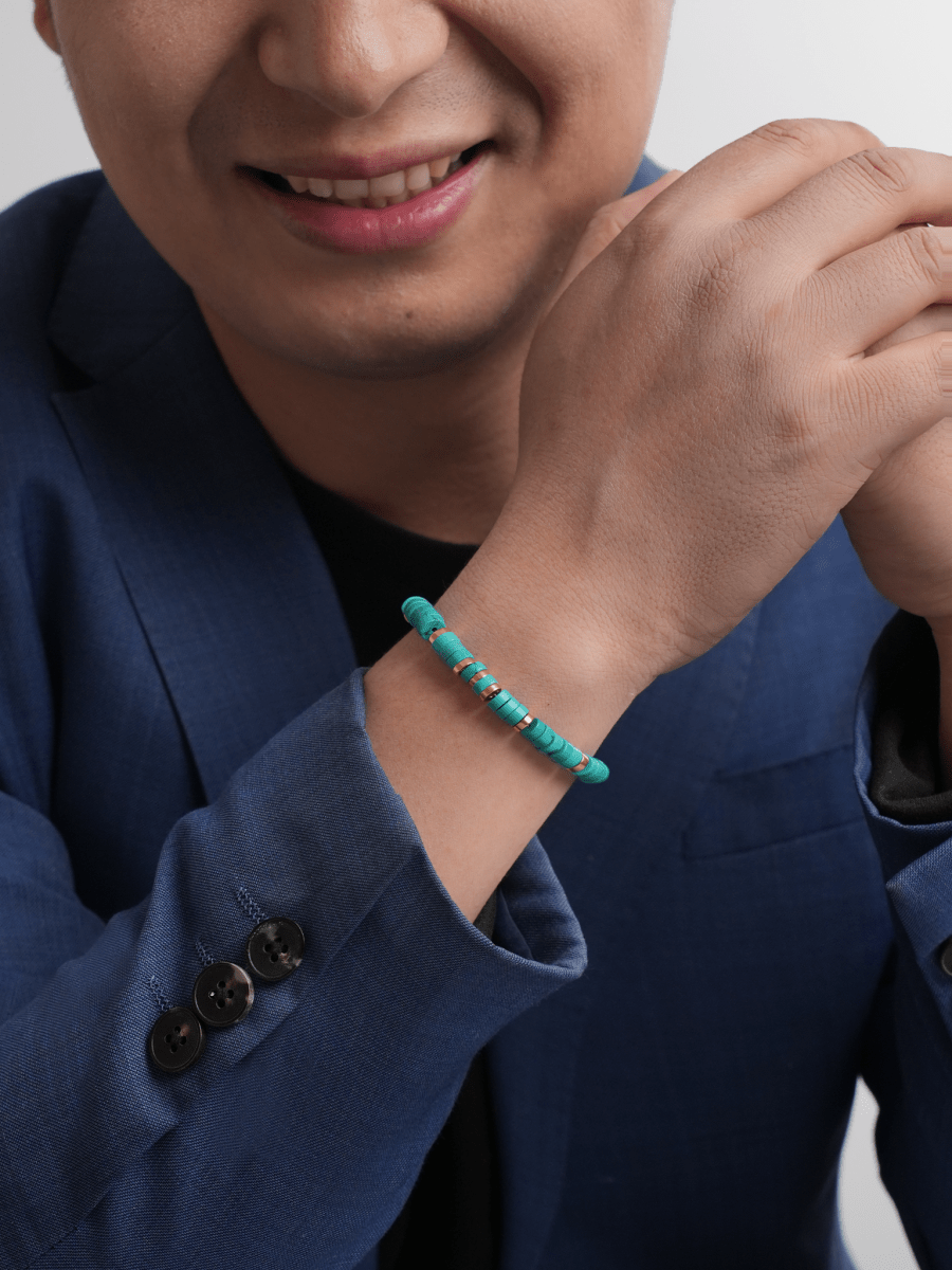 Man wearing a Turquoise & Gold-Plated Sterling Silver bracelet, promoting calm and inner peace, in a stylish blue suit.