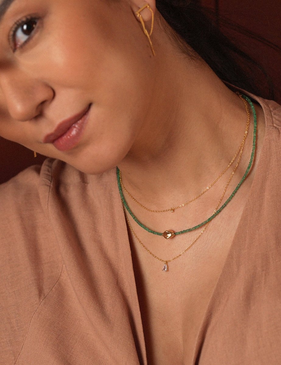 Elegant woman wearing layered emerald beaded and gold necklaces, showcasing a modern and timeless jewelry style.