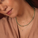 Elegant woman wearing layered emerald beaded and gold necklaces, showcasing a modern and timeless jewelry style.