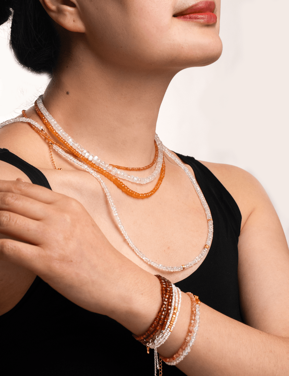 Woman wearing Success Orange Sapphire Faceted Necklace and bracelets, showcasing sparkling gemstones and elegance.