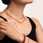 Woman wearing Success Orange Sapphire Faceted Necklace and bracelets, showcasing sparkling gemstones and elegance.