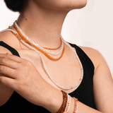 Woman wearing Success Orange Sapphire Faceted Necklace and bracelets, showcasing sparkling gemstones and elegance.