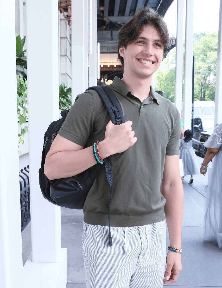 Young man wearing a green polo shirt, holding a black backpack, showcasing a stylish bracelet.