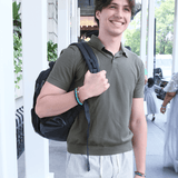 Young man wearing a green polo shirt, holding a black backpack, showcasing a stylish bracelet.