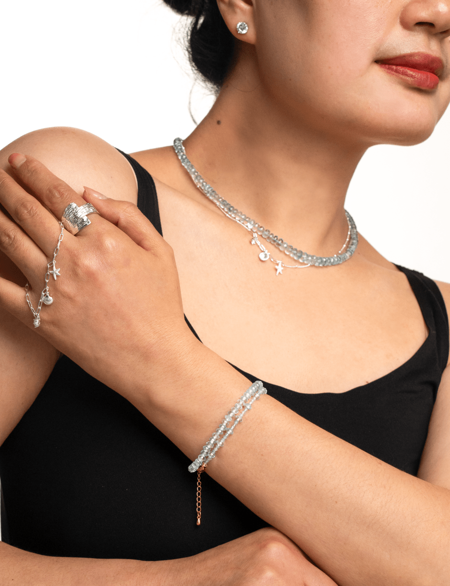 Woman wearing a multi-layer aquamarine bracelet, silver jewelry, and a pendant neckpiece, showcasing elegant minimalist style.