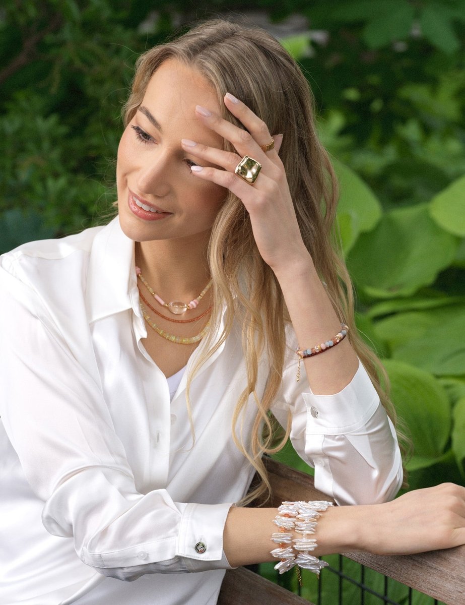 Woman wearing layered jewelry and a ring, showcasing elegance and style in a natural setting.
